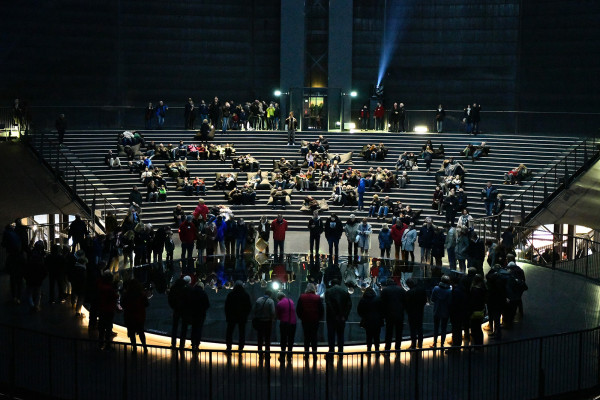Manege des Gasometers mit Zuschauern, die um einen großen Spiegel herumstehen.