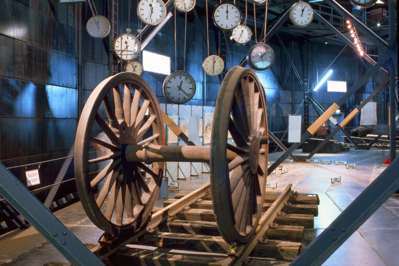 Ein alter Gleisabschnitt mit alten Gleisrädern vor von der Decke hängende Bahnhofsuhren