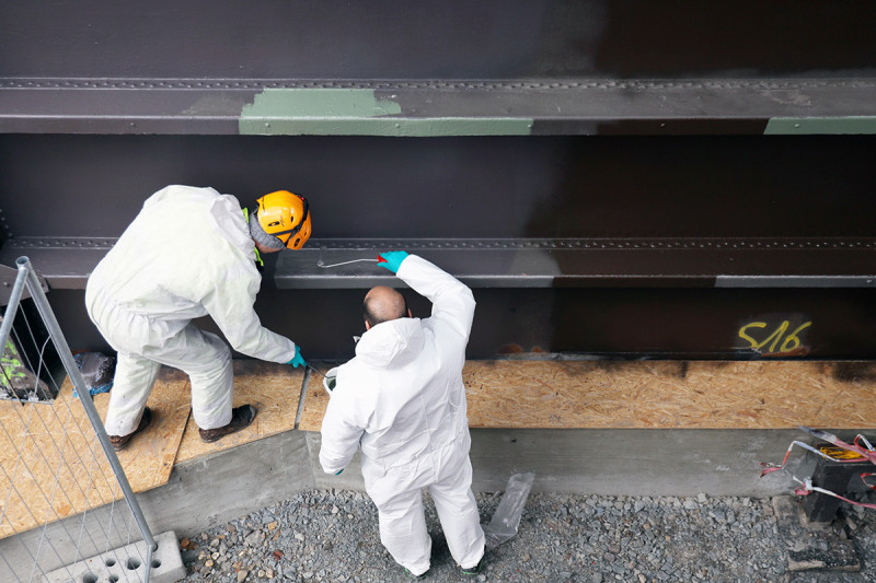Zwei Lackierer strechen die Gasometer Außenhülle mit verschiedenen Grau- und Brauntönen an.