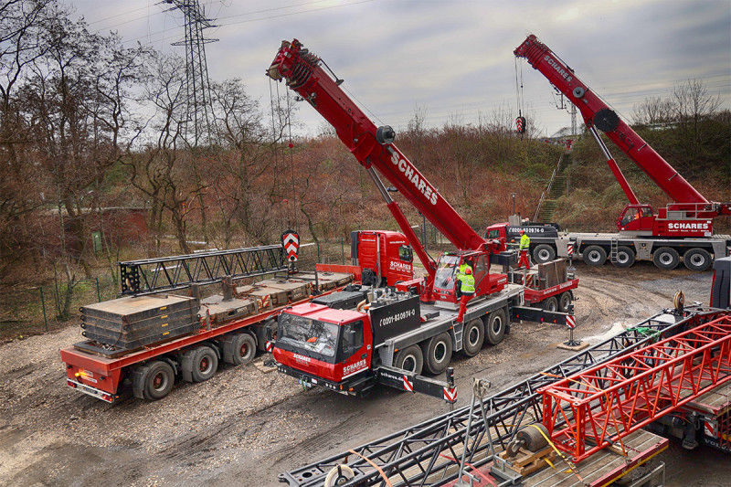 Zwei Autokräne entladen auf der Rückseite des Gasometers einen LKW.
